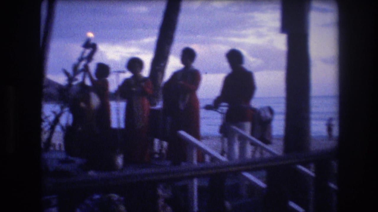 Dark silhouettes of musicians on a palm-lined seaside stage with torches and ocean beyond.