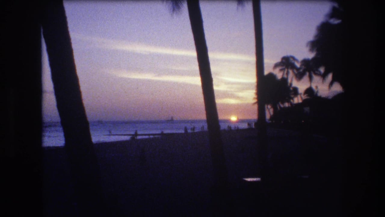 1977 Honolulu 8mm frame showing the sun near the ocean horizon, silhouetted palms, purple evening sky, and small figures along the beach.