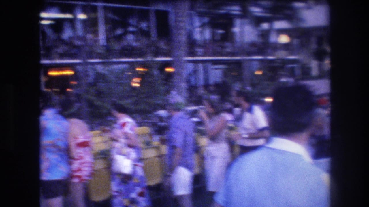 Tourists gather near yellow chairs and a glass-fronted building.
