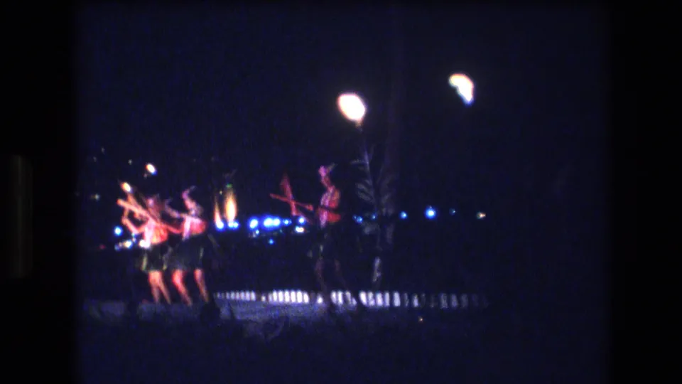1977 Honolulu frame showing a small group of hula dancers in a nighttime stage performance, with glowing overhead lamps and blue background lights.