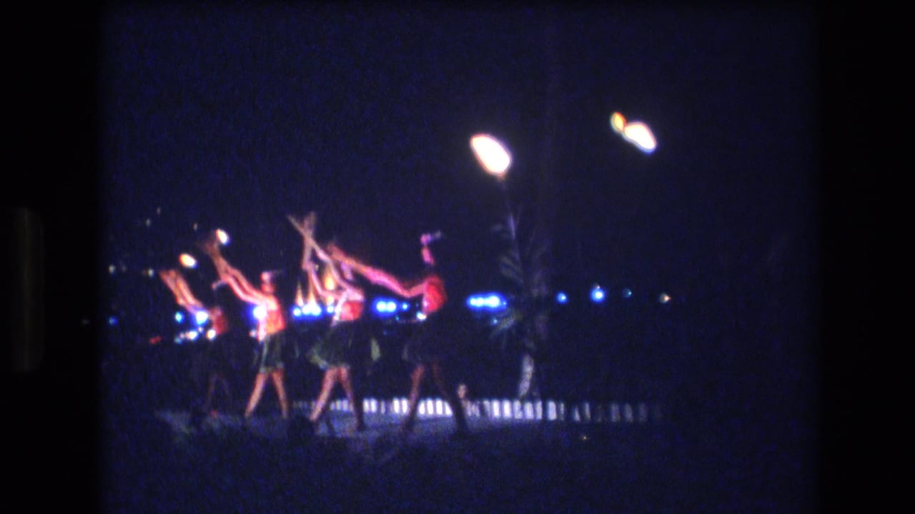 Costumed dancers raise their arms together beneath bright stage lights.