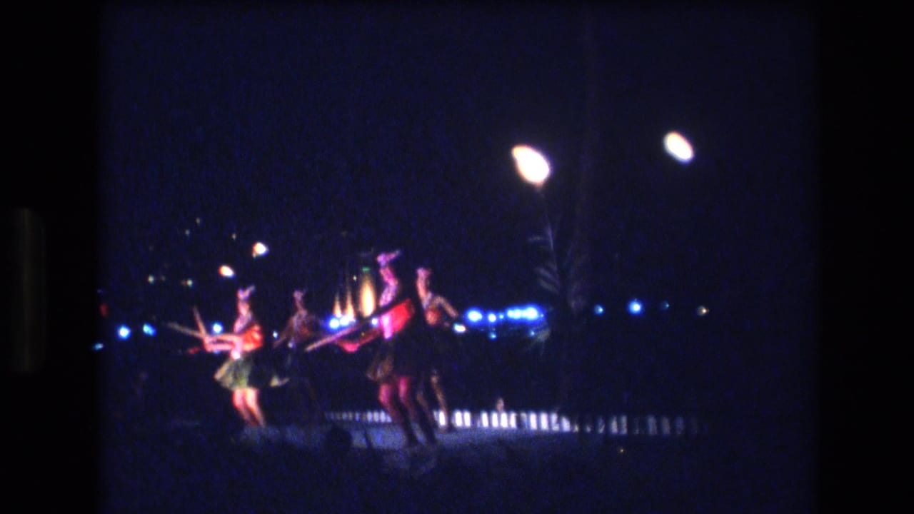 Several dancers in colorful costumes move across a nighttime stage with lamps overhead.