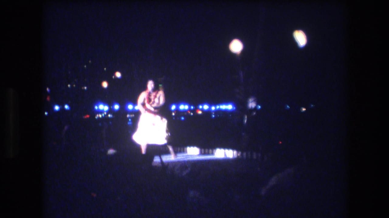 A male hula dancer in white attire and a lei performs on a small nighttime stage in Honolulu, Oahu, Hawaii, as supported by the clip metadata.