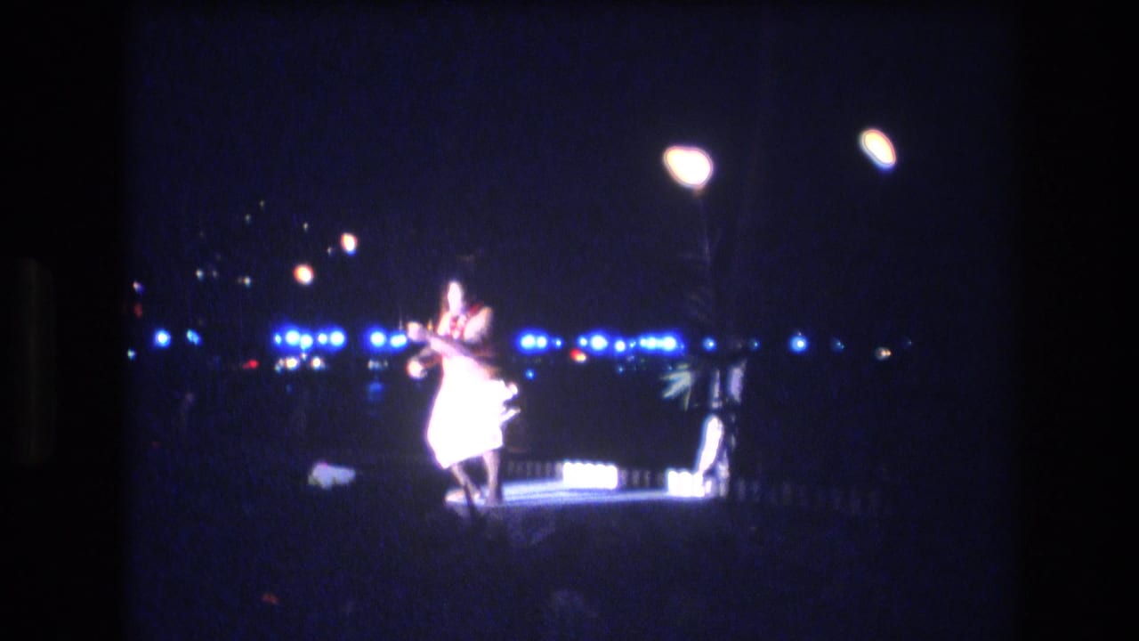 Male dancer on a small night stage under bright lamps with distant blue lights behind him.