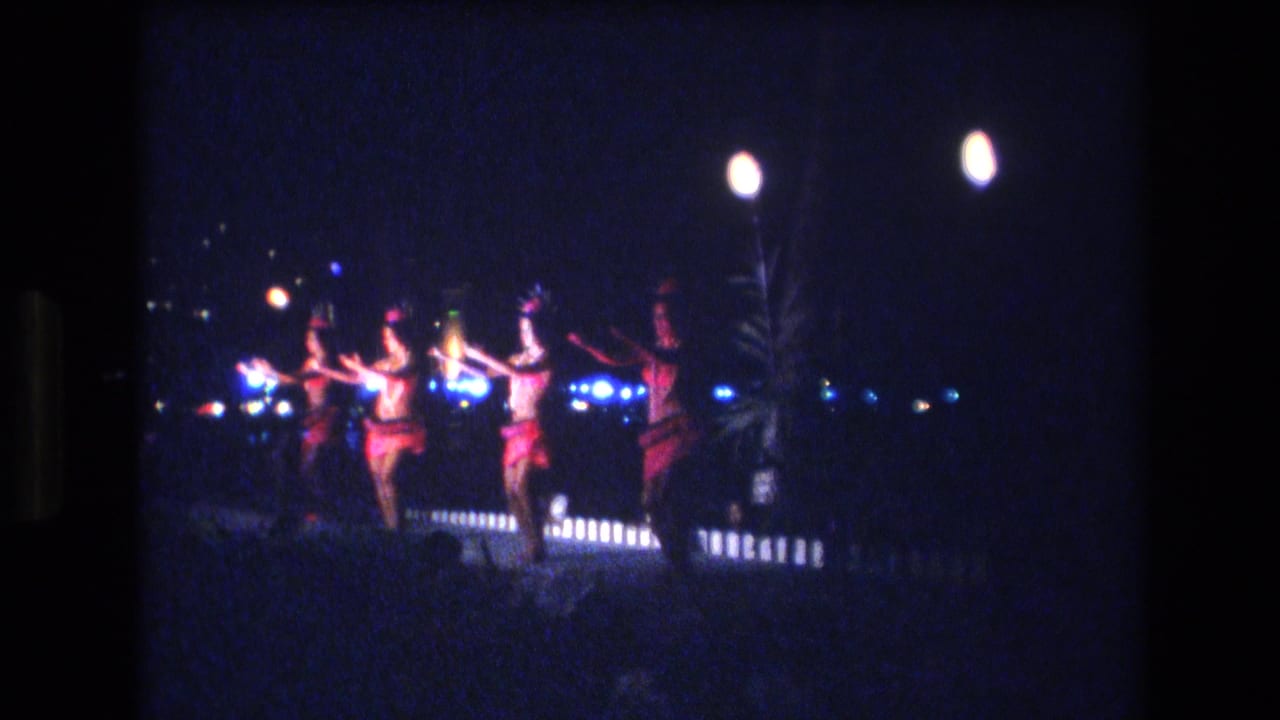 Women dance at night near bright stage lights and torches.