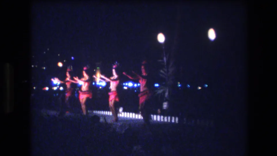 In 1977 Honolulu home-movie footage, several women appear to dance outdoors at night under blue-white lights with torch-like flames nearby.