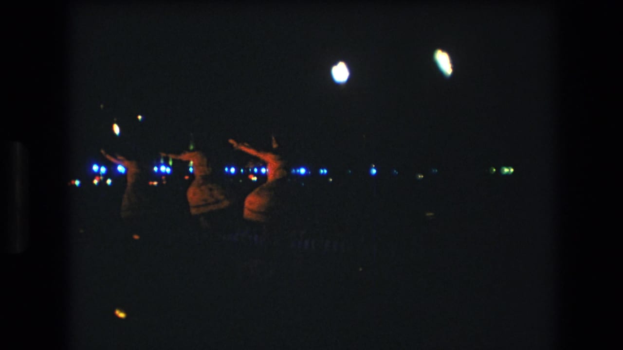 Three hula dancers are seen in dim light with bright blue points of light behind them.