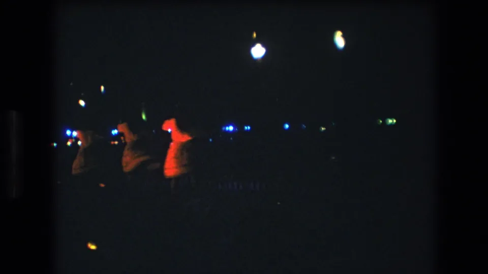 A final 1977 Honolulu frame shows three hula dancers at night, including one figure catching warmer red-orange light while blue lights remain visible in the distance.