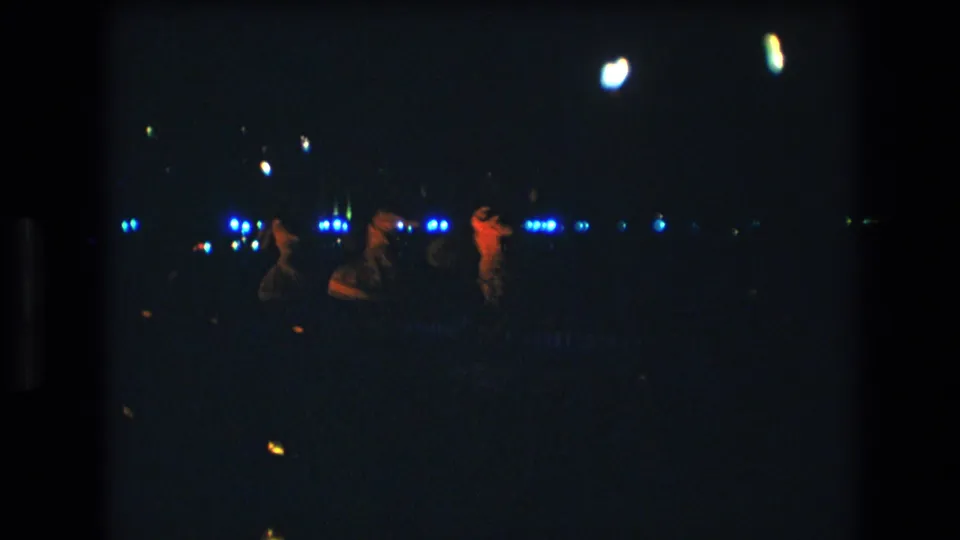 Near the end of the clip, three women continue a low-light stage dance in Honolulu, partly silhouetted against blue lights with one performer lit red.