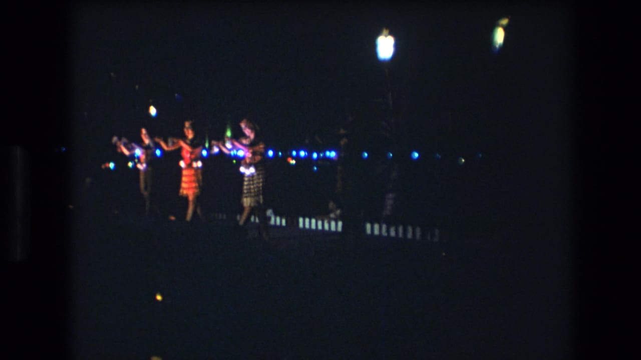 Several women perform a synchronized dance with raised arms during a nighttime Honolulu, Oahu scene recorded on 8mm footage in 1977.