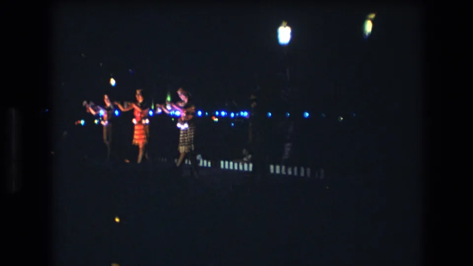 Several women perform a synchronized dance with raised arms during a nighttime Honolulu, Oahu scene recorded on 8mm footage in 1977.