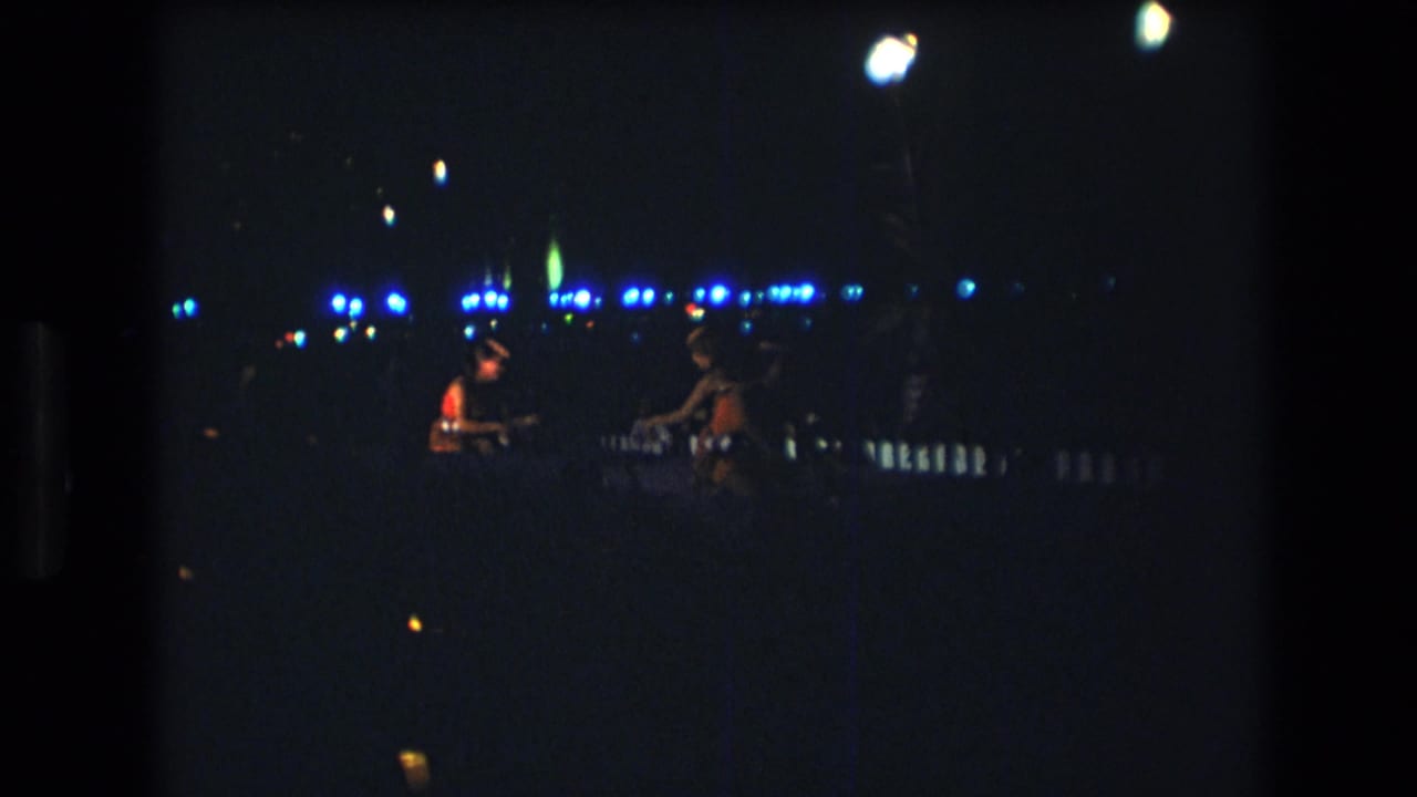 Two distant performers or musicians silhouetted against blue lights at night.