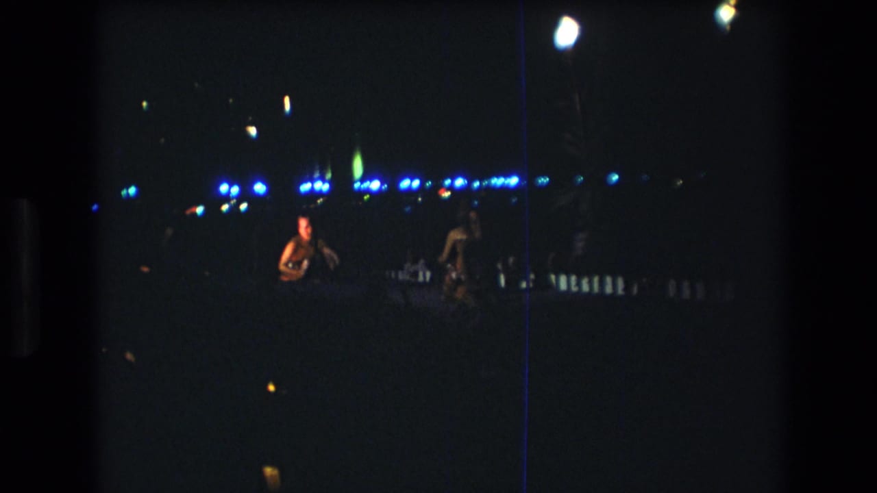 Two performers stand apart on a dark stage with blue lights behind them.