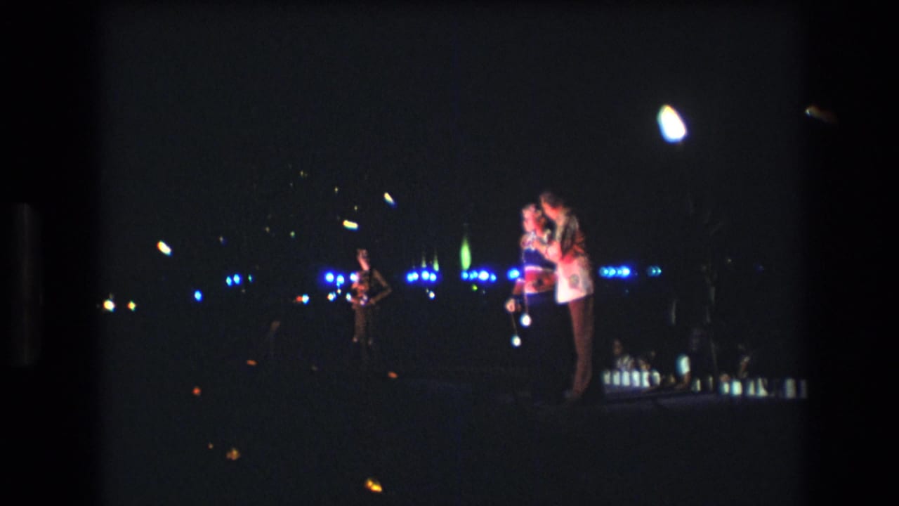 Two performers sing together under bright overhead and blue stage lights.