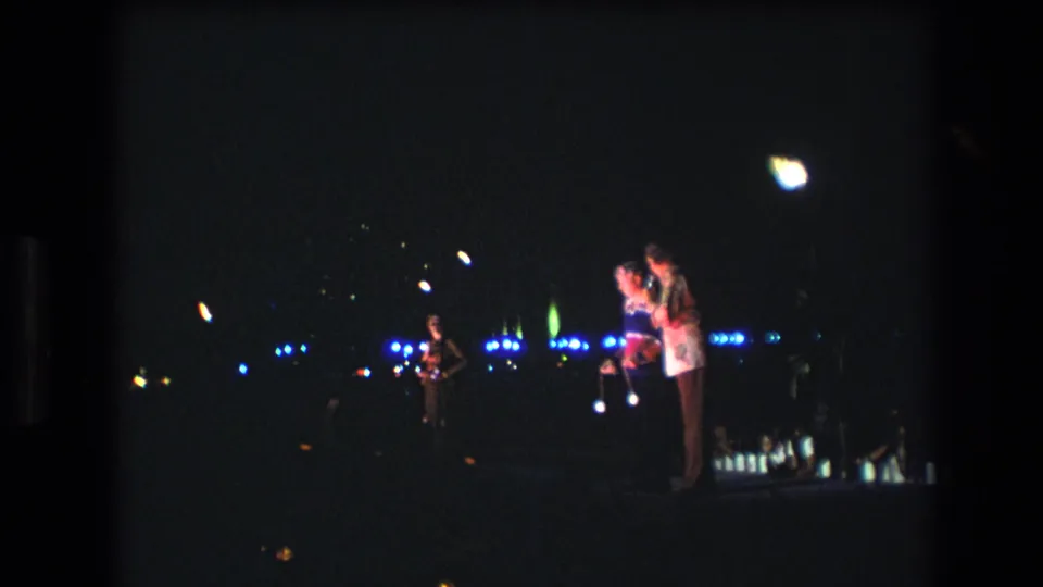 The final frame shows the couple at right in a dark 1977 Honolulu home-movie scene, with another person farther back and scattered lights across the background.
