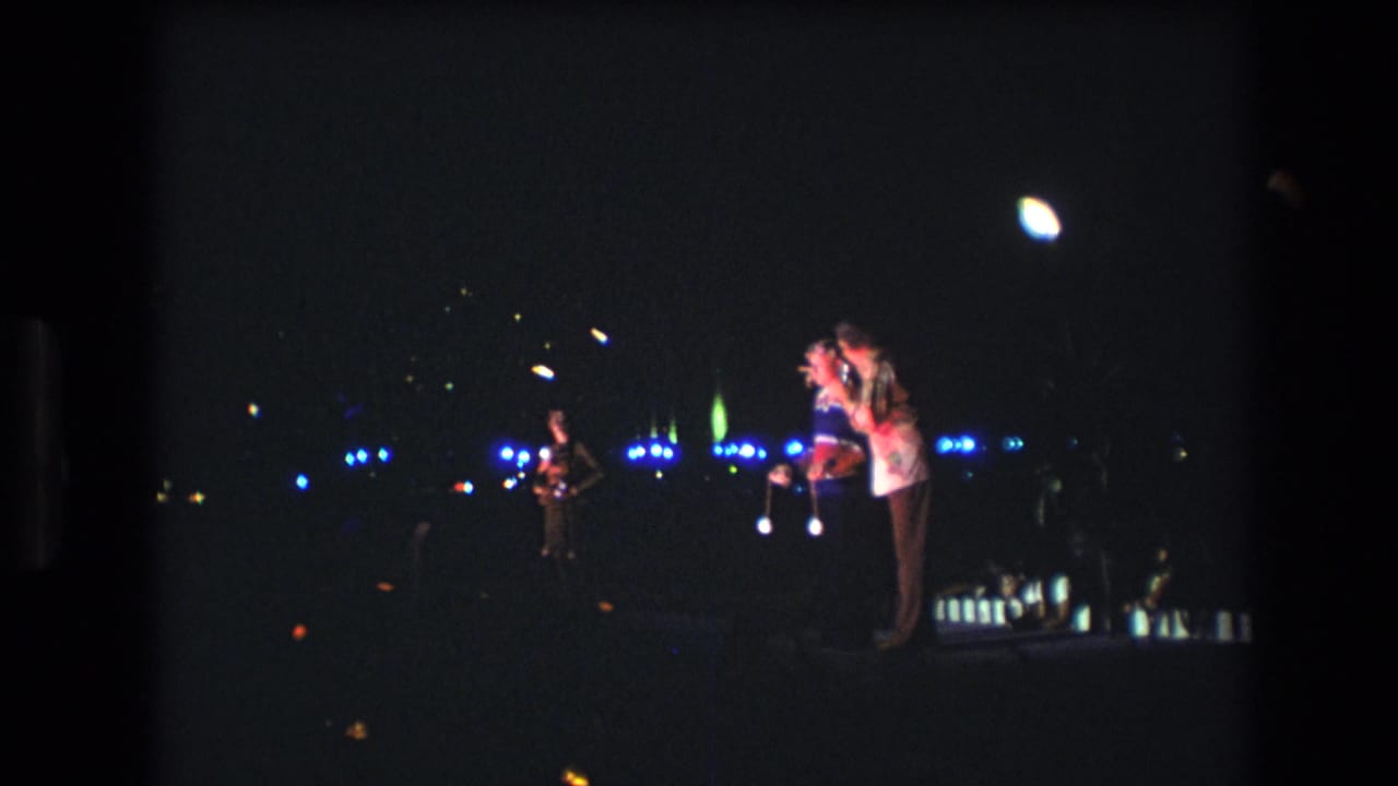 A woman and two men appear on a dimly lit stage with blue lights across the background.