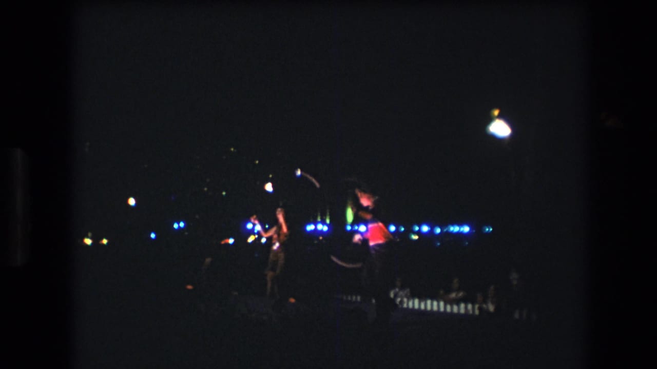 Two women perform with batons against blue night lights.
