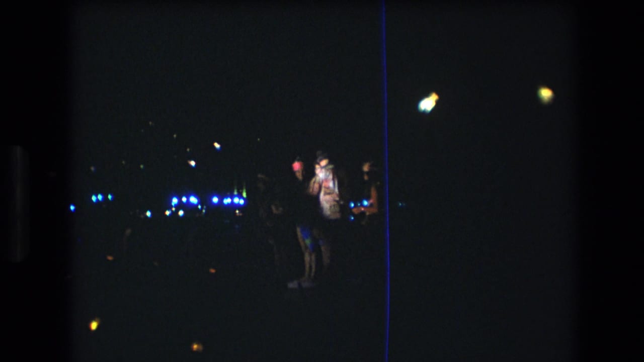 Two people near the center-right with distant blue lights in the dark background.