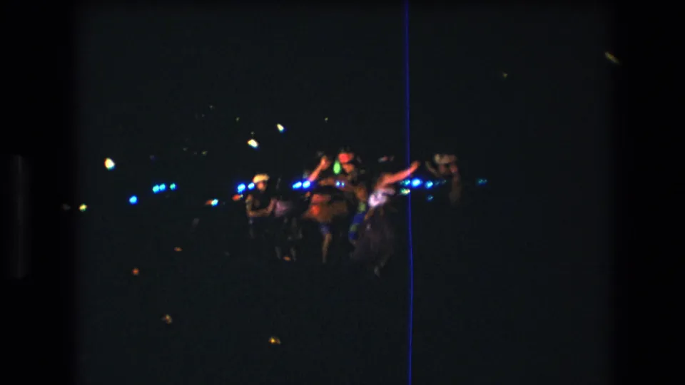 1977 Honolulu home-movie frame showing a small group dancing energetically at night, with arms raised and blue lights behind them.