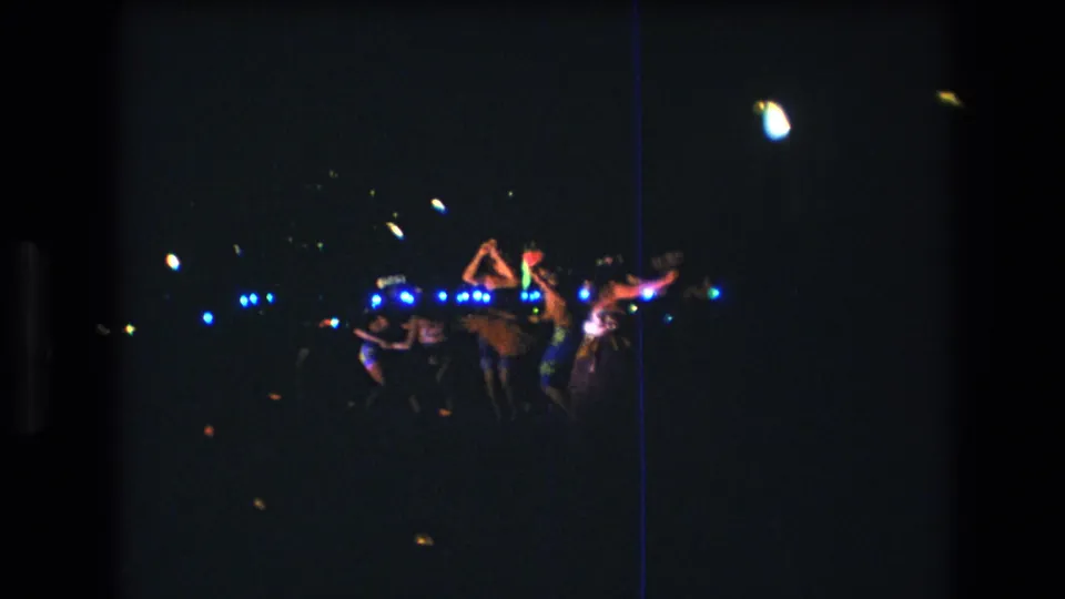 1977 Honolulu dance party frame with several people moving together under scattered blue and yellow lights in a grainy night scene.
