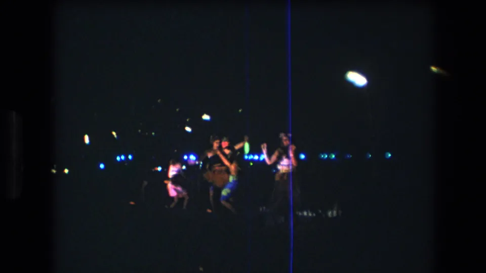 Final 1977 Honolulu frame showing dancers in traditional-style attire near center stage, with blue and green lights and strong low-light 8mm grain.