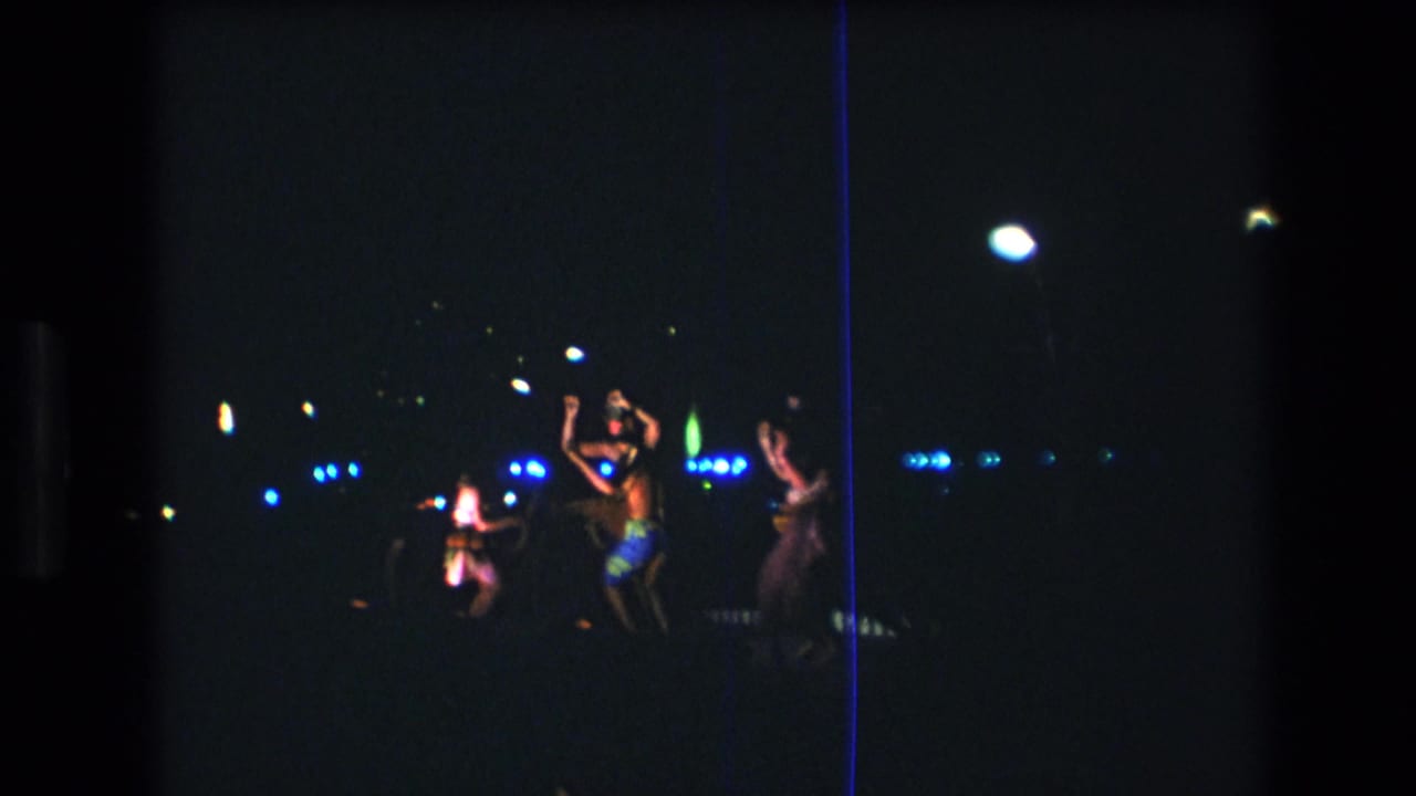 Several women appear to dance during a dark nighttime performance in Honolulu, Hawaii, with blue lights and torchlike highlights visible in the distance.