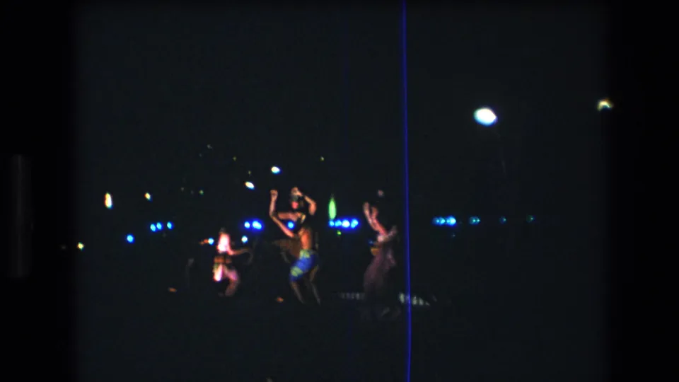 Several women appear to dance during a dark nighttime performance in Honolulu, Hawaii, with blue lights and torchlike highlights visible in the distance.
