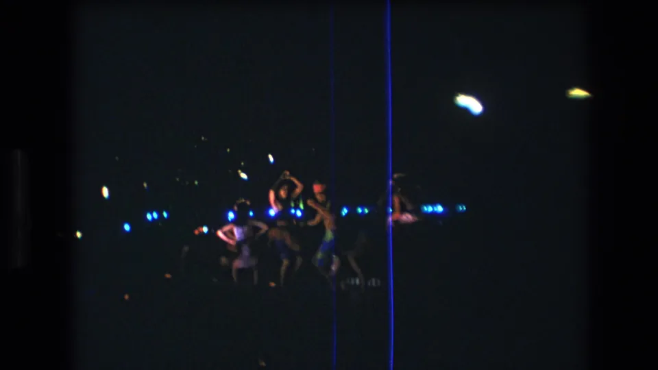 Women continue a nighttime dance sequence in Honolulu, with one or more figures raising their arms amid dark staging, blue light points, and visible film scratches.
