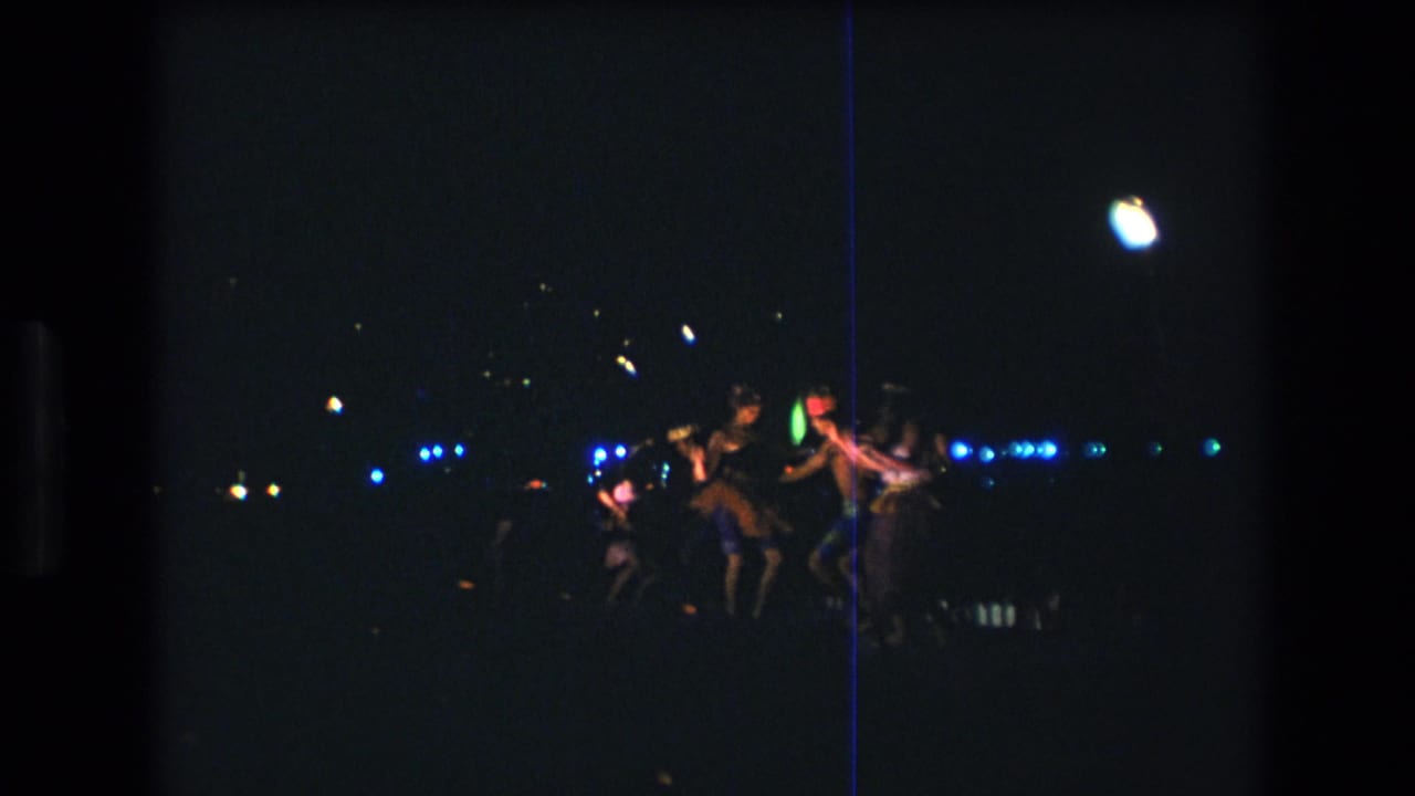 Group of adults dancing in a dark outdoor setting with blue lights across the background.