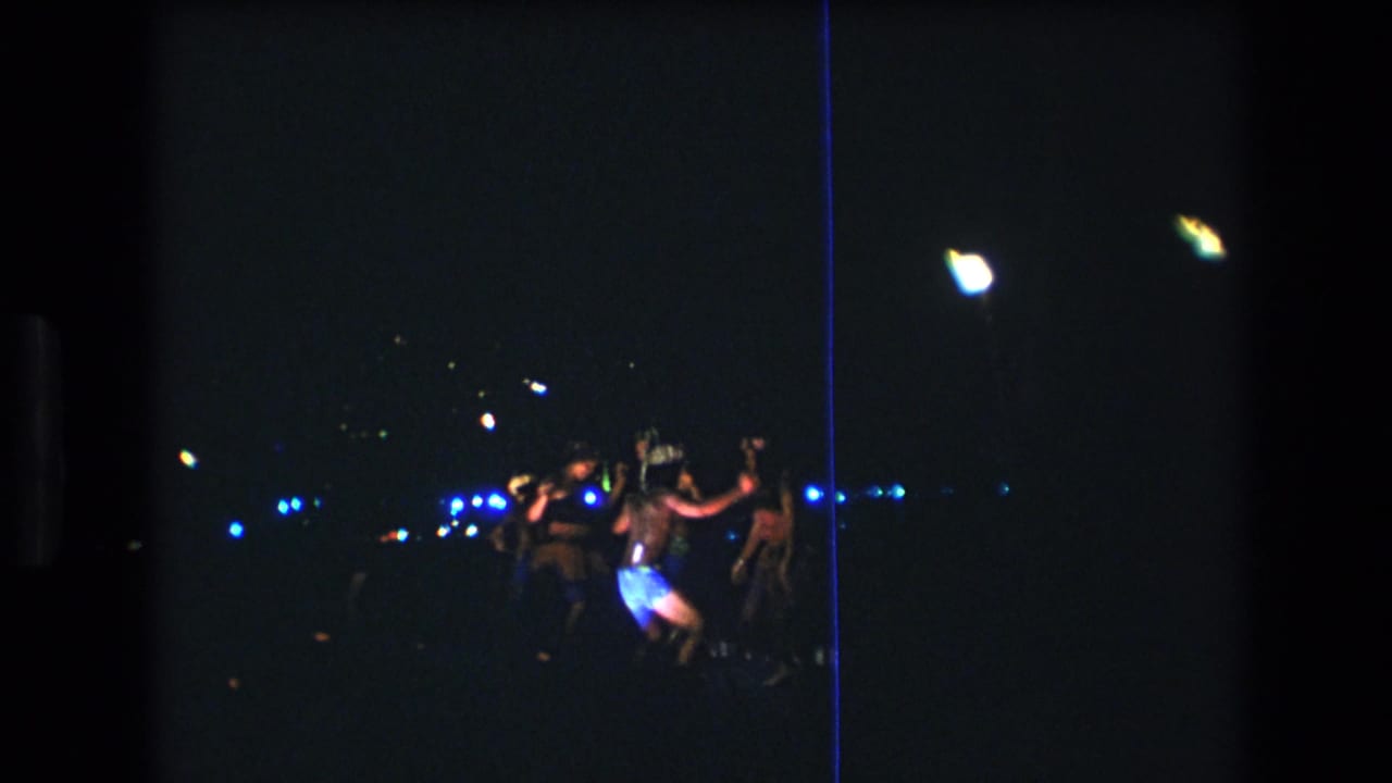 1977 8mm home-movie frame from Oahu showing a small group of luau dancers at night, seen from a distance in very low light.