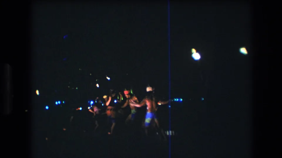 Nighttime Oahu luau performance captured on 8mm film, with several dancers in island-style clothing silhouetted against scattered blue and white lights.