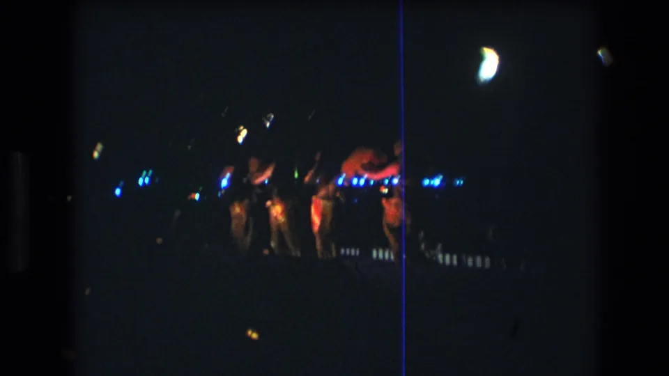 Low-light 1977 home-movie frame of a luau dance group on Oahu, with performers partly blurred by motion and darkness.