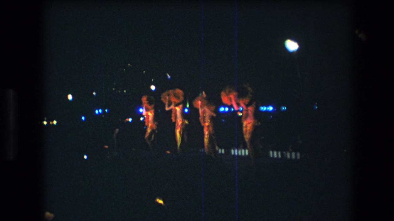 Dancers continue a synchronized routine on a dark stage with blue light points behind them.