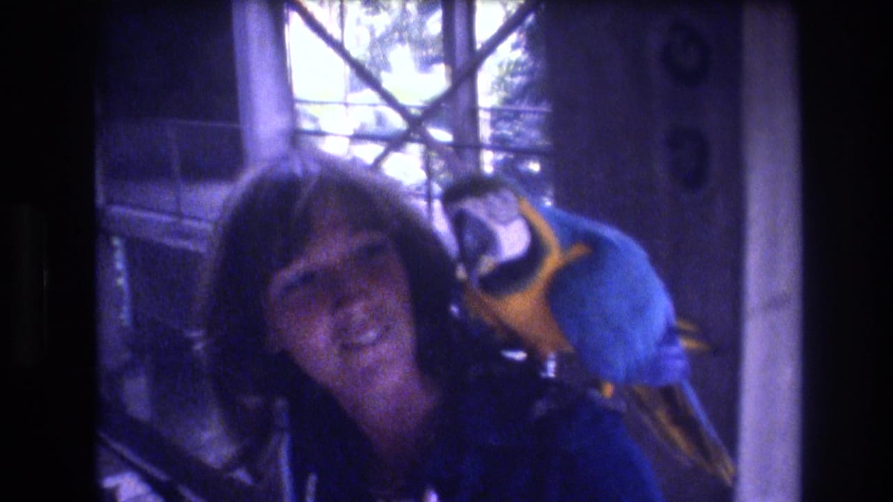 Woman looking toward the camera with a macaw perched beside her head.