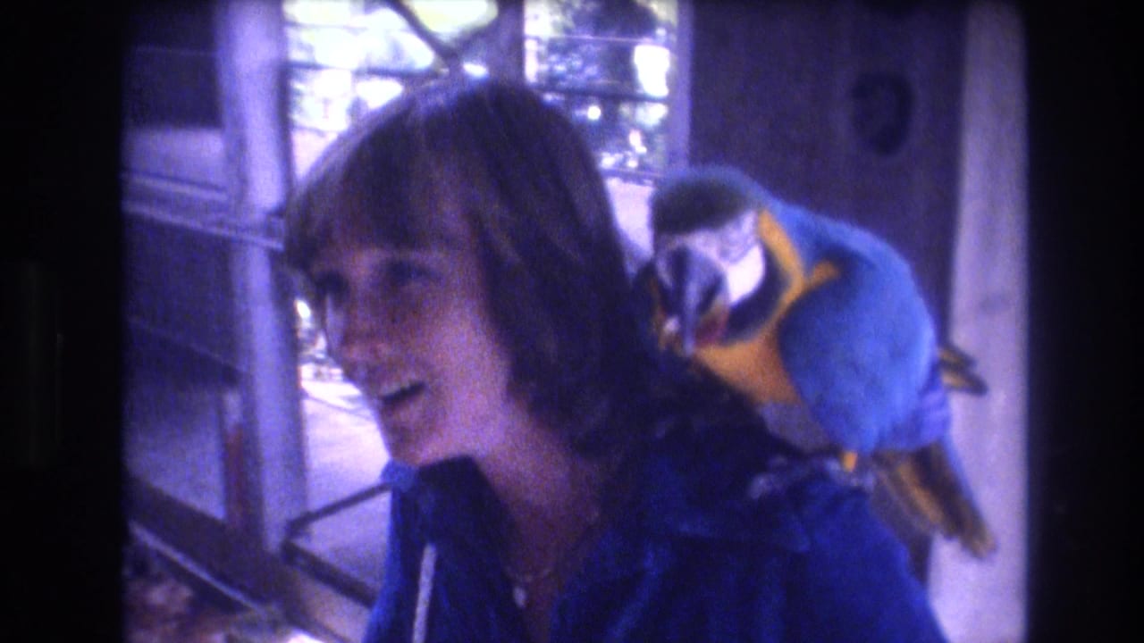 Woman smiling with a blue-and-yellow macaw perched behind her shoulder.