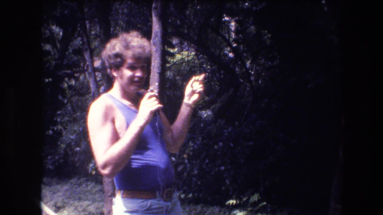 Man with microphone raises one hand while standing near trees.