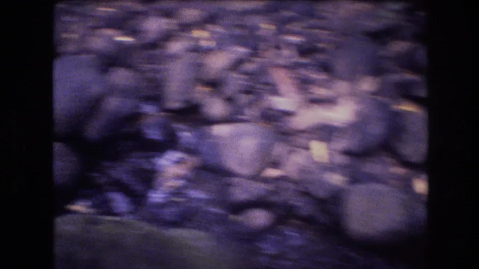 1977 Honolulu, Oahu 8mm frame with rounded stream stones and shallow water seen through handheld motion blur and aged color shift.