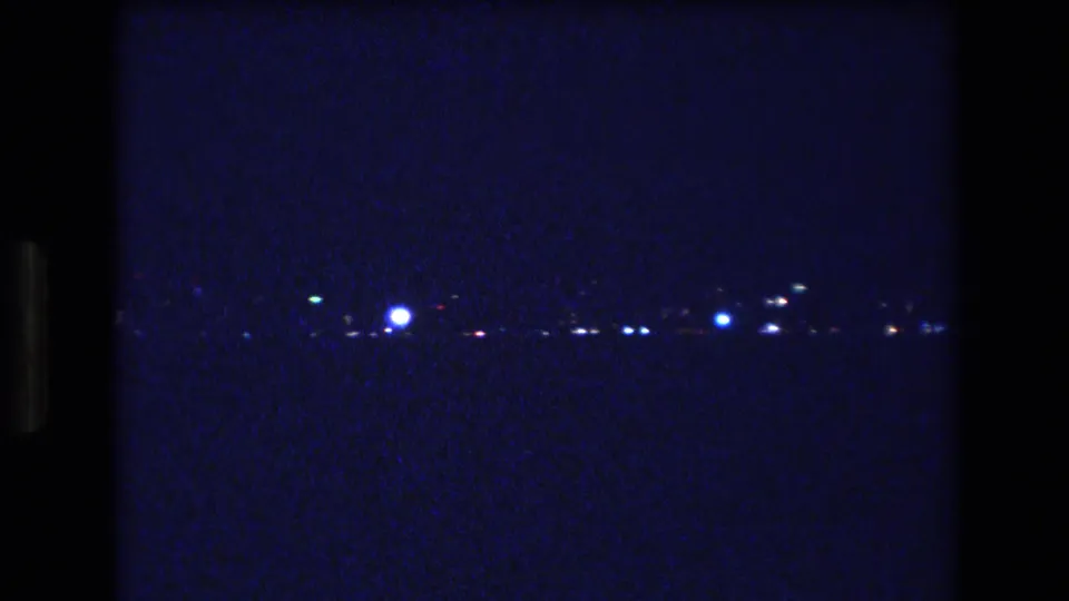 1977 Honolulu or Oahu 8mm frame showing a low band of distant lights across a mostly black night landscape.