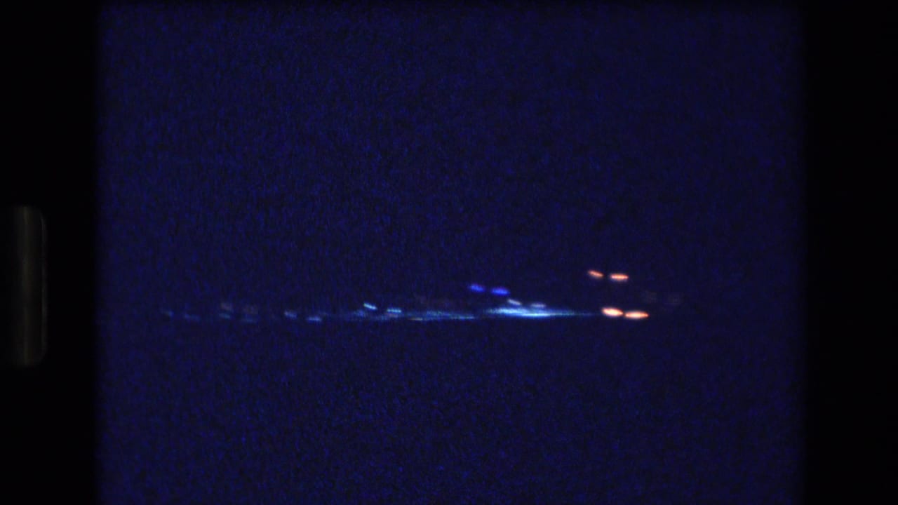 A grainy 1977 Honolulu night view frames distant city lights as blue-white and red points across a dark waterfront horizon.