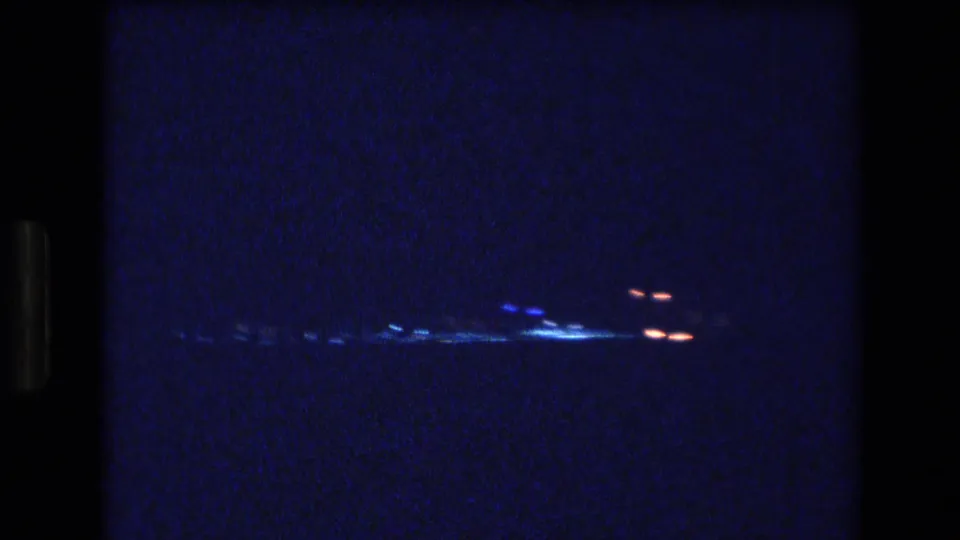 A grainy 1977 Honolulu night view frames distant city lights as blue-white and red points across a dark waterfront horizon.