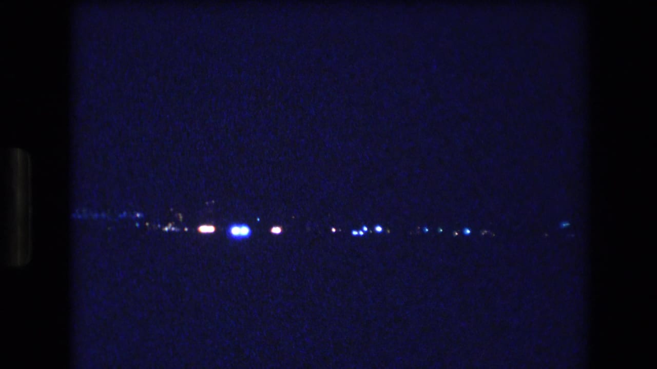 1977 Honolulu, Oahu home-movie frame showing scattered distant blue and white lights against a dark, grainy blue night exposure.