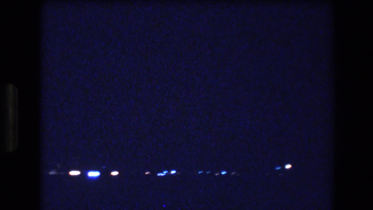 Small blue and white lights sit low across a dark grainy night scene.