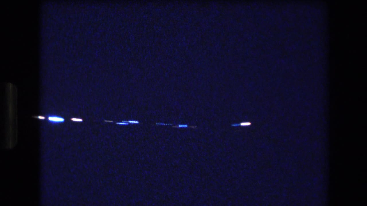 Dark, blue-tinted 8mm frame from the supplied 1977 Honolulu home-movie clip, with scattered points of light and little visible interior detail.