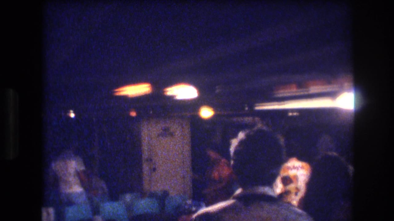 Adults seen from behind and in profile inside a dim room with lounge seating.