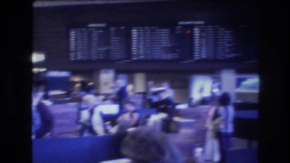 Travelers wait and move through a Honolulu airport terminal area in 1977, with flight information boards above counters and soft blue 8mm lighting.