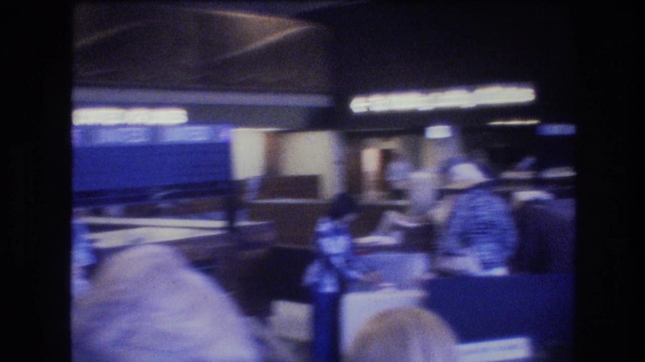 Passengers pass through a dimly lit airport concourse in Honolulu, with a counter area, overhead illuminated signage, and 1970s traveler clothing visible.