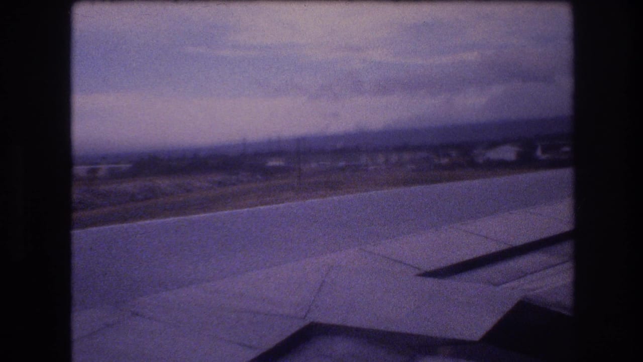 Airplane-window view over Honolulu, Oahu, with the wing in the foreground and the runway, low buildings, and cloudy sky beyond.