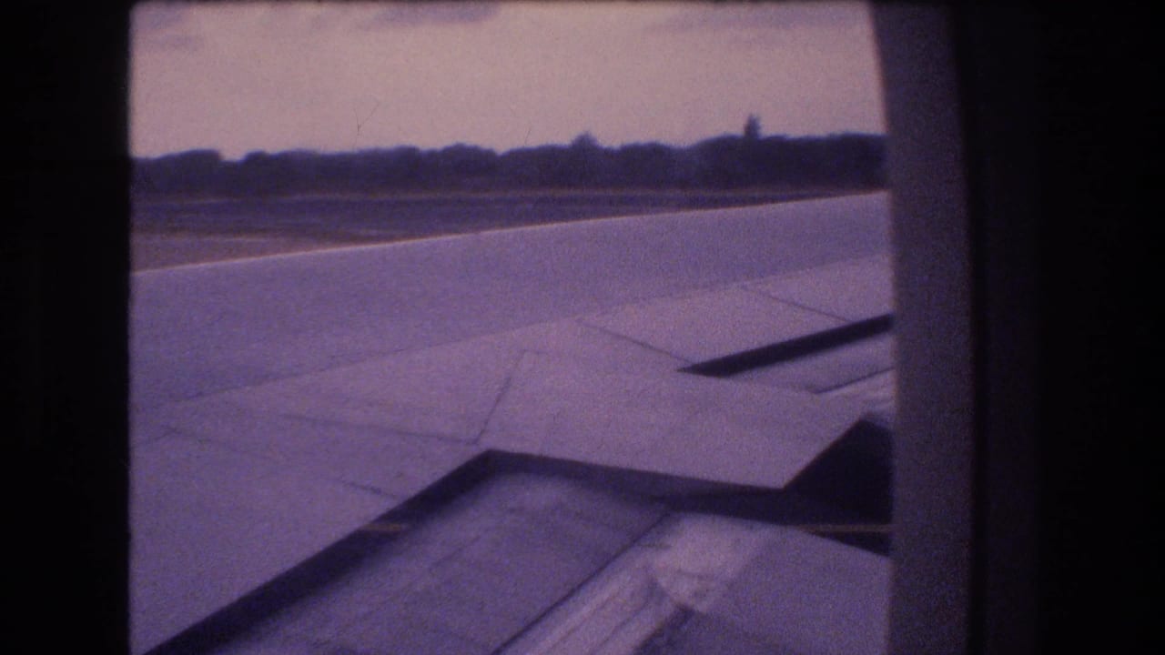 1977 Honolulu, Oahu passenger-window view of an airplane wing over runway pavement, with a low treeline and hazy sky in the distance.