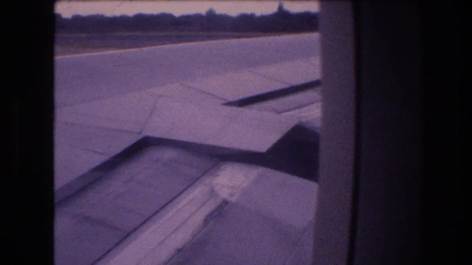 1977 Honolulu, Oahu 8mm frame with the aircraft wing filling the lower view and runway pavement stretching toward a distant treeline.