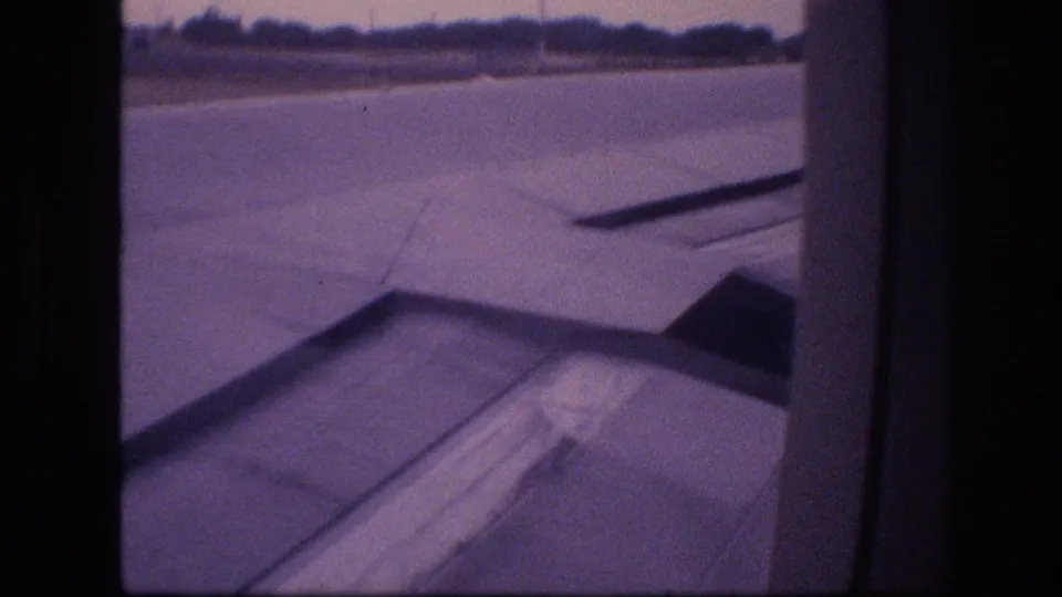 Soft 8mm frame of an airplane wing and runway from a passenger-window perspective during takeoff or landing in the supplied 1977 Honolulu travel footage.